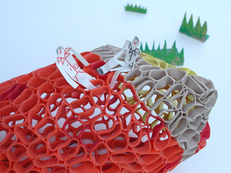 Close up of red and grey rubberband sculptures with paper figures and fake grass.