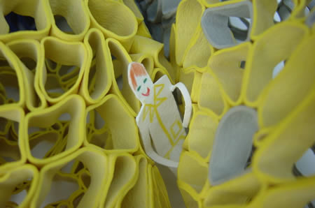 Close up of yellow rubberband sculpture with paper figure.